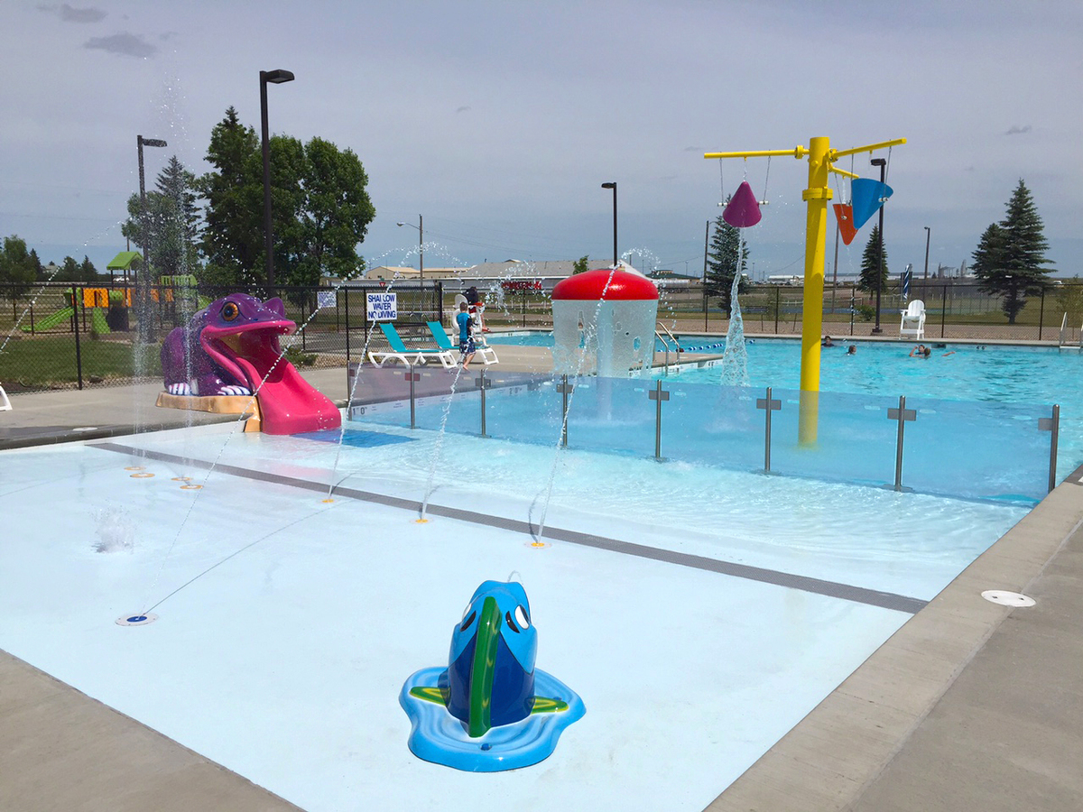 Tioga Municipal Pool's outdoor lap/leisure pool with zero depth beach entry, a frog water slide, barrier wall, dumping buckets, and spray features